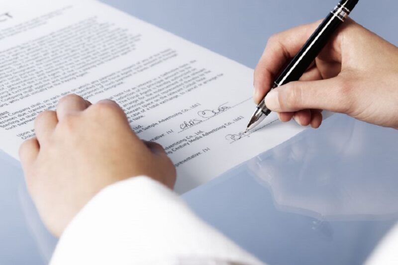 Close up of woman signing a legal document or contract, blank background.