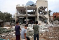 Palestinian stare at a mosque-turned-shelter in Deir al-Balah in the central Gaza Strip, heavily damaged in an Israeli strike during the night of October 6, 2024, amid the ongoing war between Israel and the Palestinian Hamas movement. Gaza's civil defence agency said on October 6 that an Israeli strike on the mosque-turned-shelter in central Deir al-Balah killed 21 people, while Israel's military said it had targeted Hamas militants. (Photo by BASHAR TALEB / AFP)